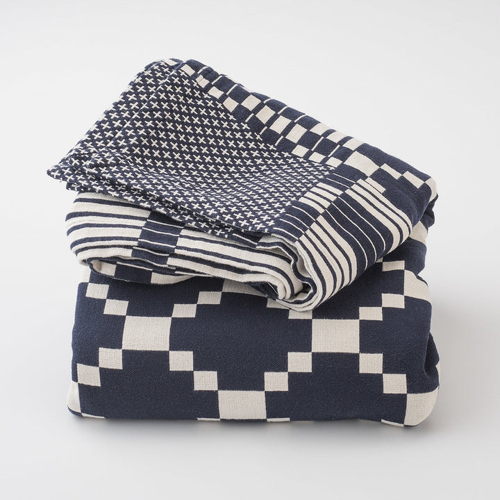 Folded Winter and Summer Cotton Coverlet showing navy and white woven geometric and striped patterns on white background