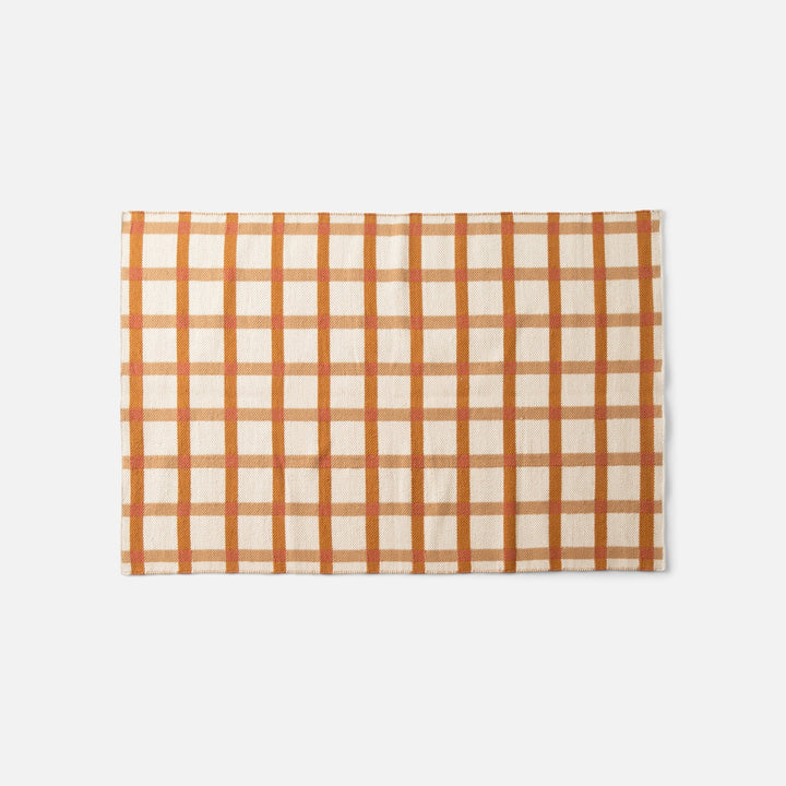 Overhead view of Plaid Wool Reversible Rug showcasing orange and cream high-contrast plaid, handwoven natural-dyed wool on white background