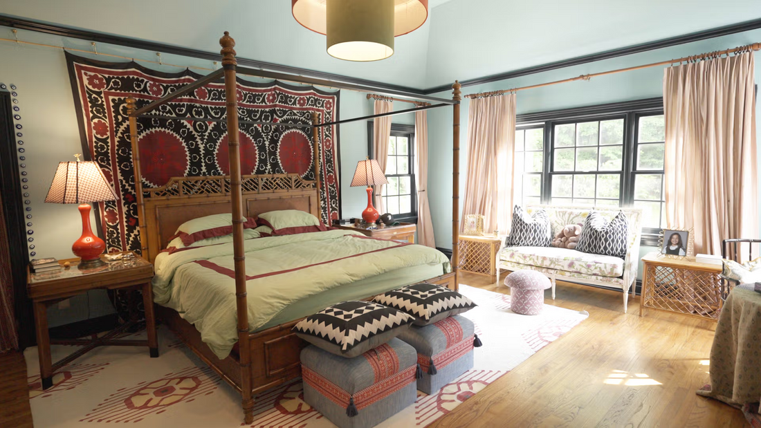 Four-poster bed in an eclectic sunlit bedroom with patterned tapestry, mint walls, red bedside lamps, and a window seat