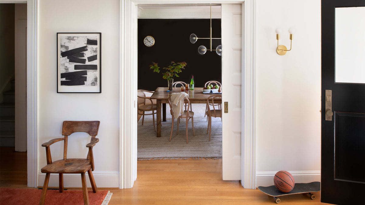 Entryway looking into dining room with wooden table, bentwood chairs, brass light, and skateboard with ball by black door