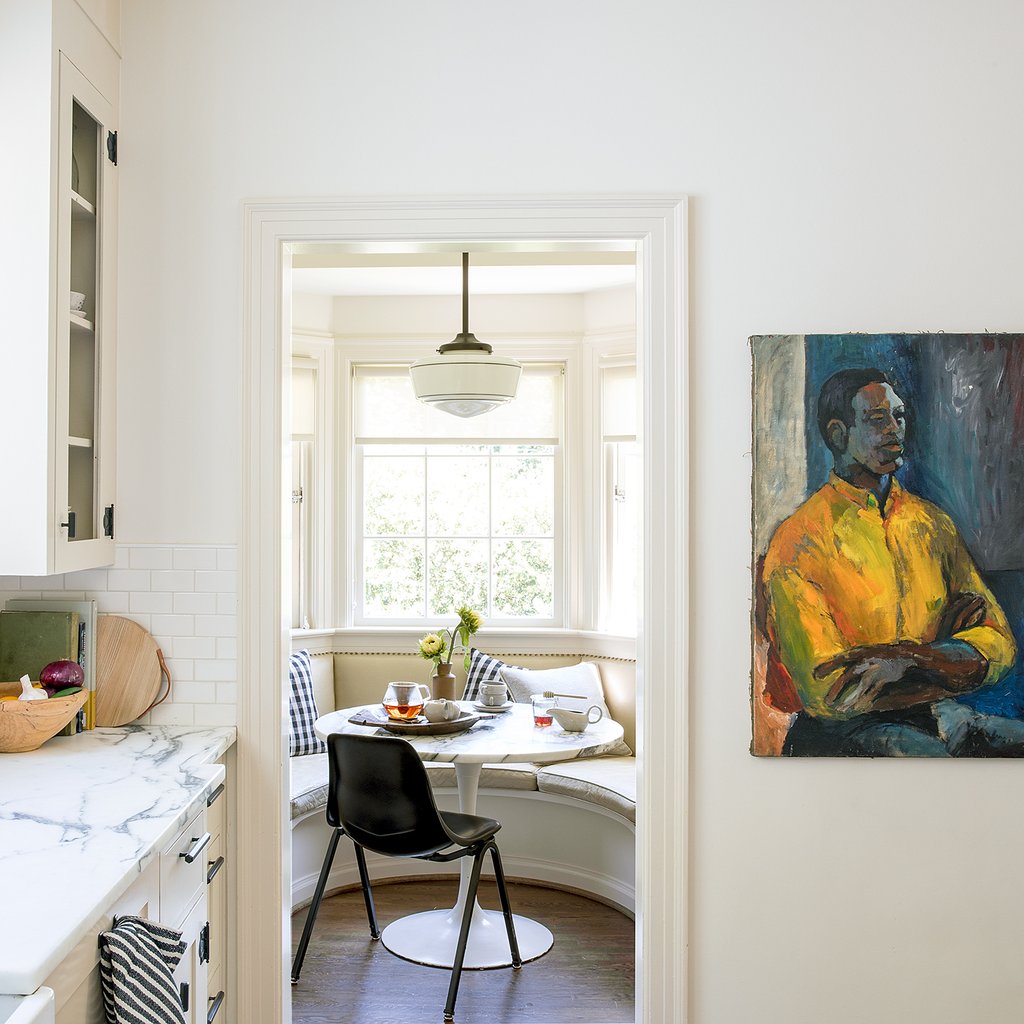Pendant light over a round breakfast-nook table in a bright kitchen, with built-in banquette and a portrait on the wall
