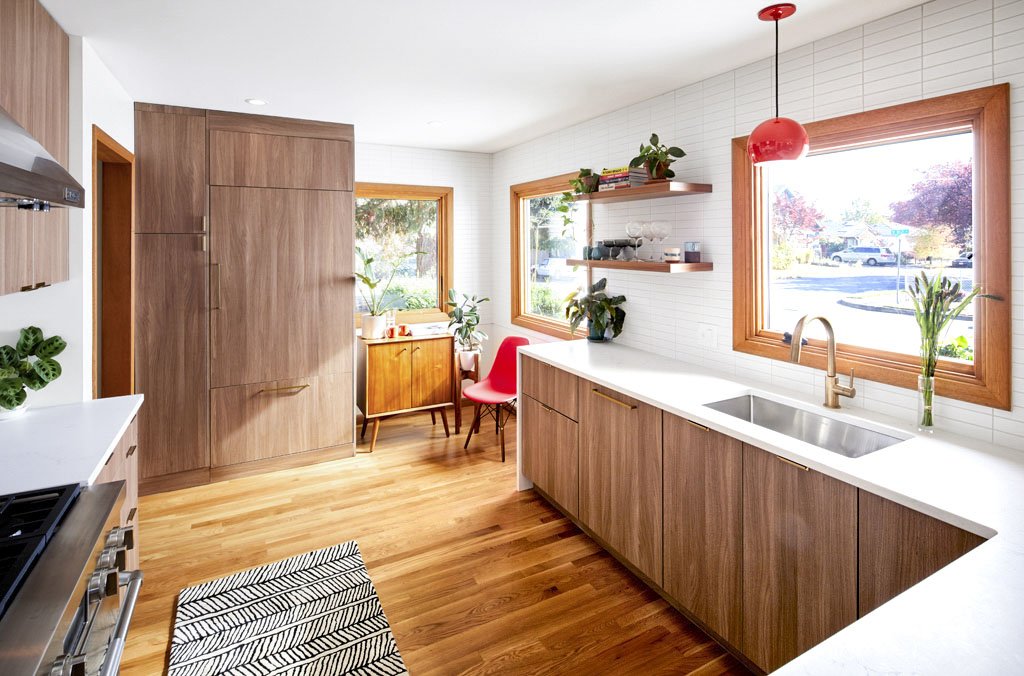 Sunlit midcentury modern kitchen with walnut cabinets, white countertops, stainless sink, red pendant light and hardwood floors
