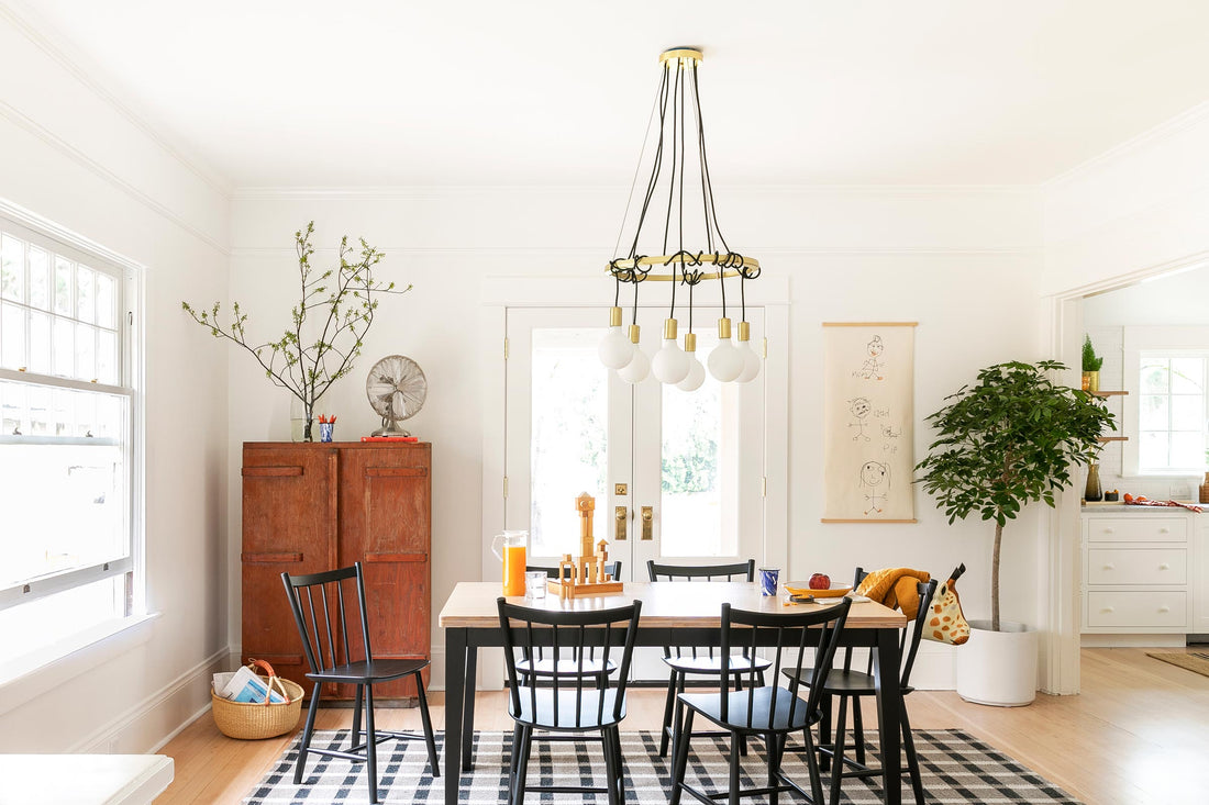 Brass multi-bulb chandelier hanging over wooden dining table with black chairs in a bright white dining room