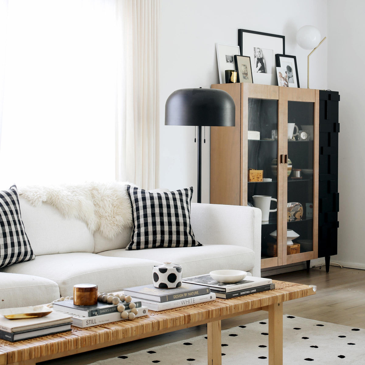 Neutral, light-filled living room with white sofa, black-and-white plaid pillows, rattan coffee table, and black dome floor lamp