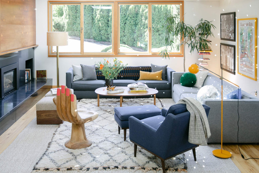 Living room with two floor lamps lighting a cozy seating area with blue sofas, a wooden hand chair, coffee table, and large window