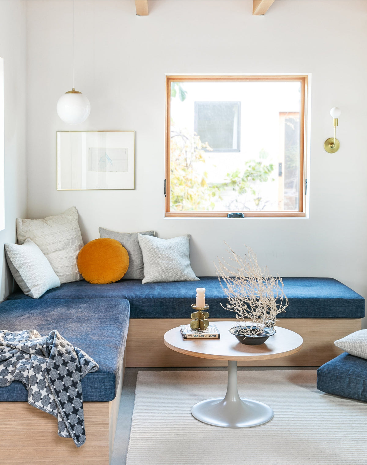 Built-in daybed under a window in a bright neutral nook with blue cushions, a mustard round pillow and a small coffee table