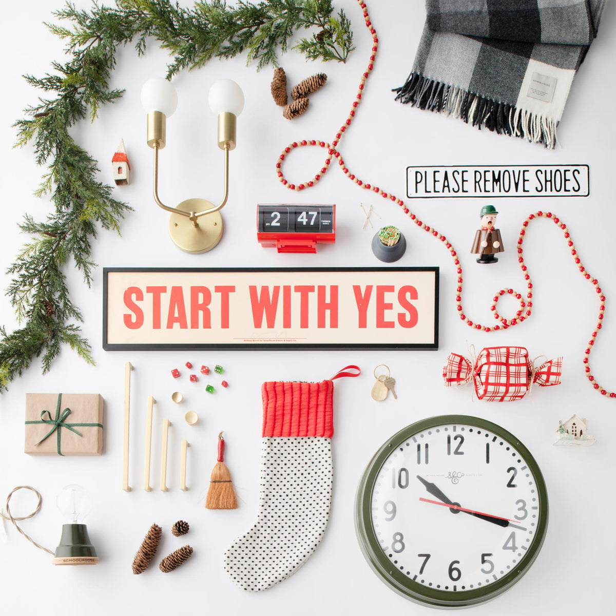 Flatlay of holiday gifts around framed Start With Yes sign, featuring wall clock, brass sconce, plaid scarf, plaid stocking