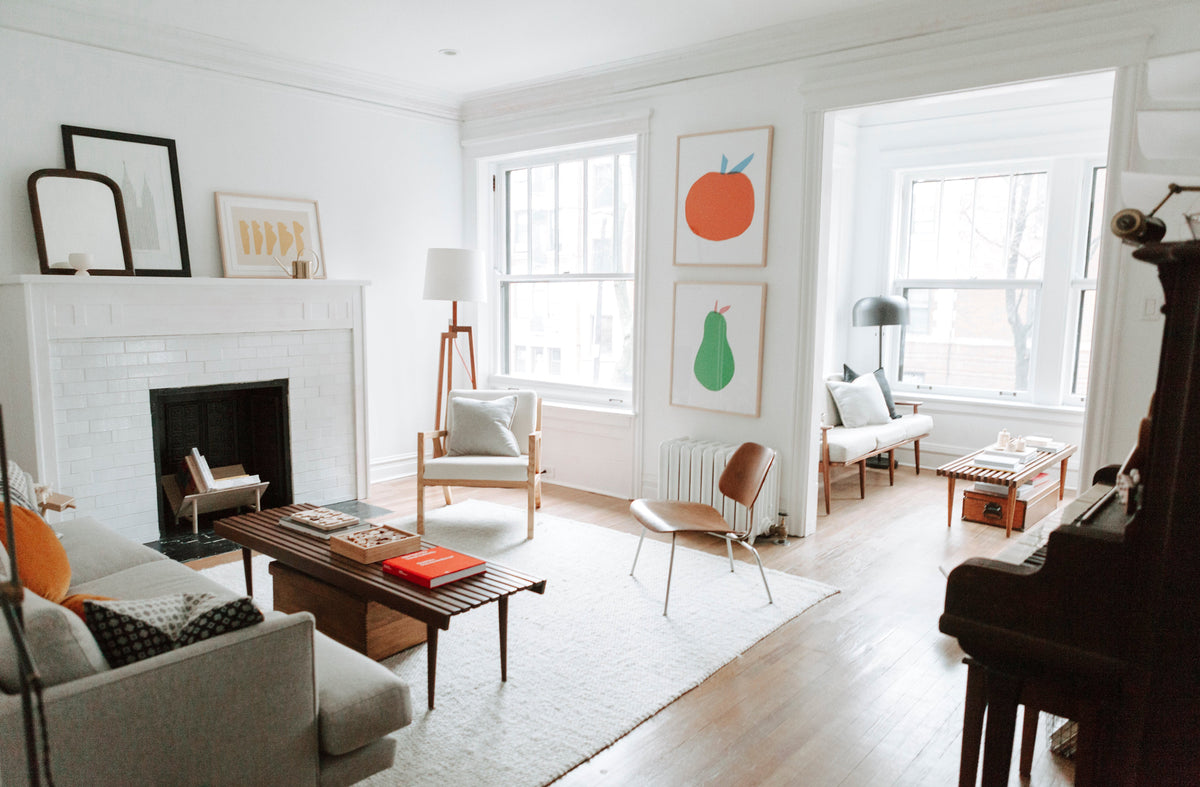 Bright Chicago living room with white fireplace, mid-century wood furniture, large windows, and framed orange and pear prints