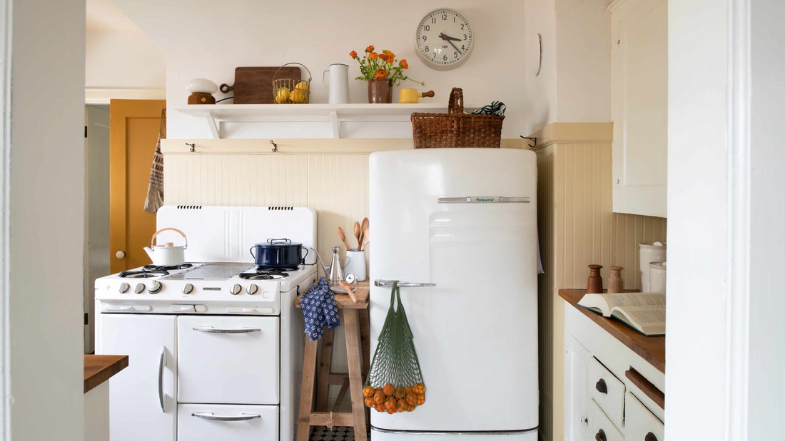 Sunlit vintage kitchen with white gas stove and retro refrigerator, mesh bag of oranges hanging from the fridge and an open cookbook on the wood counter