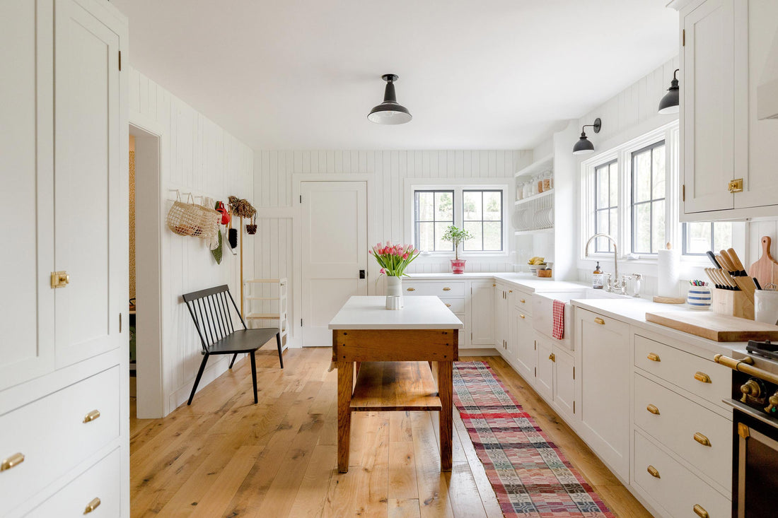 Bright farmhouse kitchen with white cabinets, wooden island with tulips, brass pulls, black sconce lights and wood floors