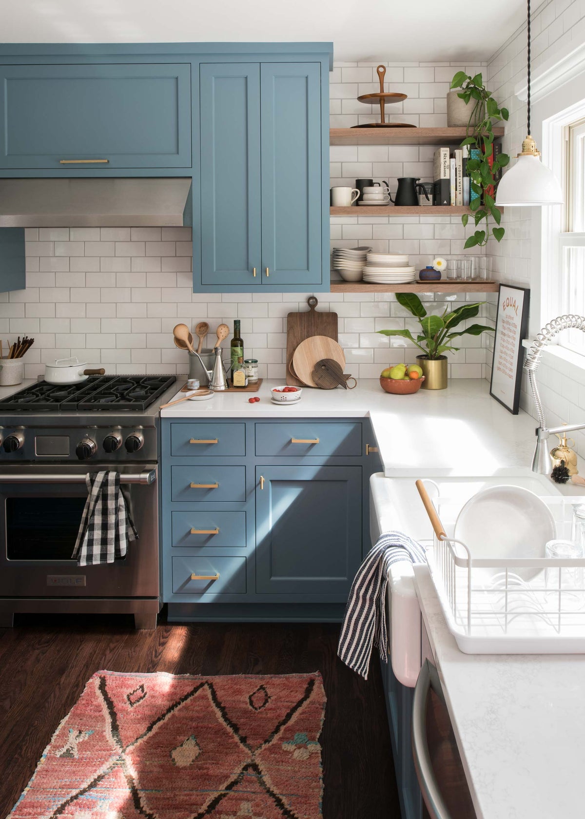 Blue cabinets beside a stainless range and open wood shelves with dishes on a subway-tile backsplash in a kitchen