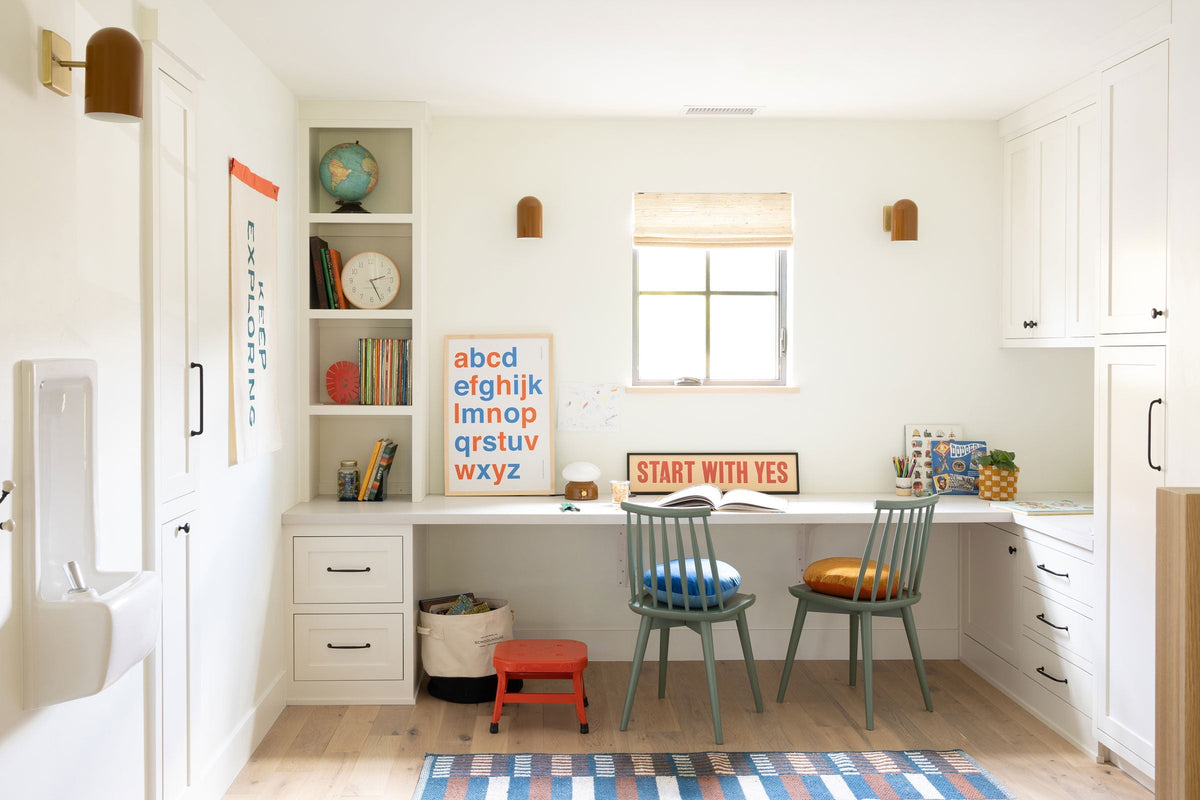 Two children’s chairs at a built-in study desk in a bright homework nook with an alphabet poster and START WITH YES sign