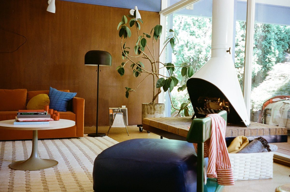 1970s-inspired living room with orange sofa, white tulip coffee table, cone fireplace, floor lamp, potted plant, and patterned rug