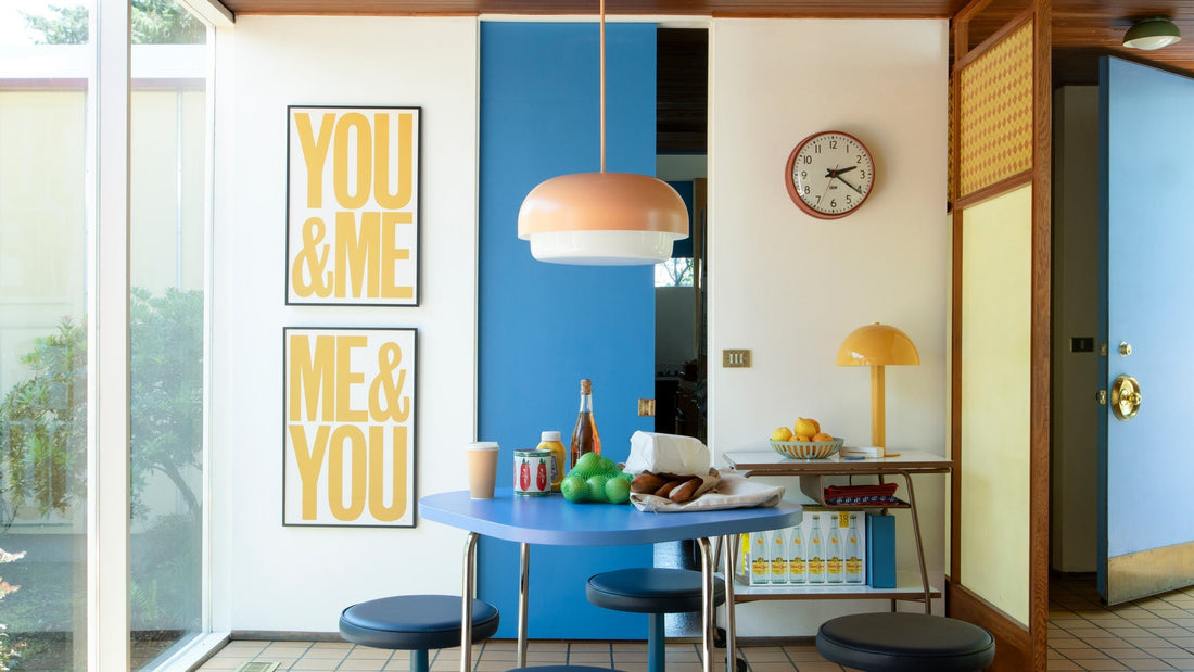 Peach dome pendant light hanging over a blue mid-century dining table with yellow YOU and ME wall prints