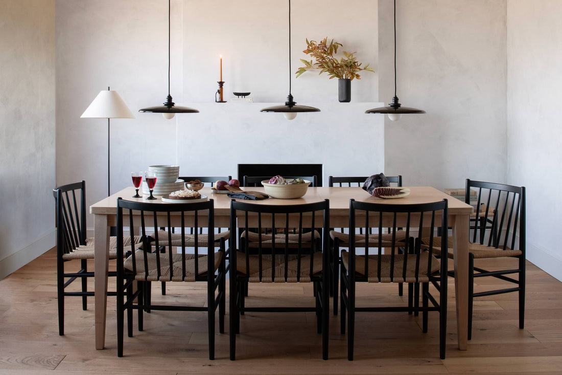 Dining table set for meal with eight black spindle-back chairs and three low black pendant lights in a minimalist dining room