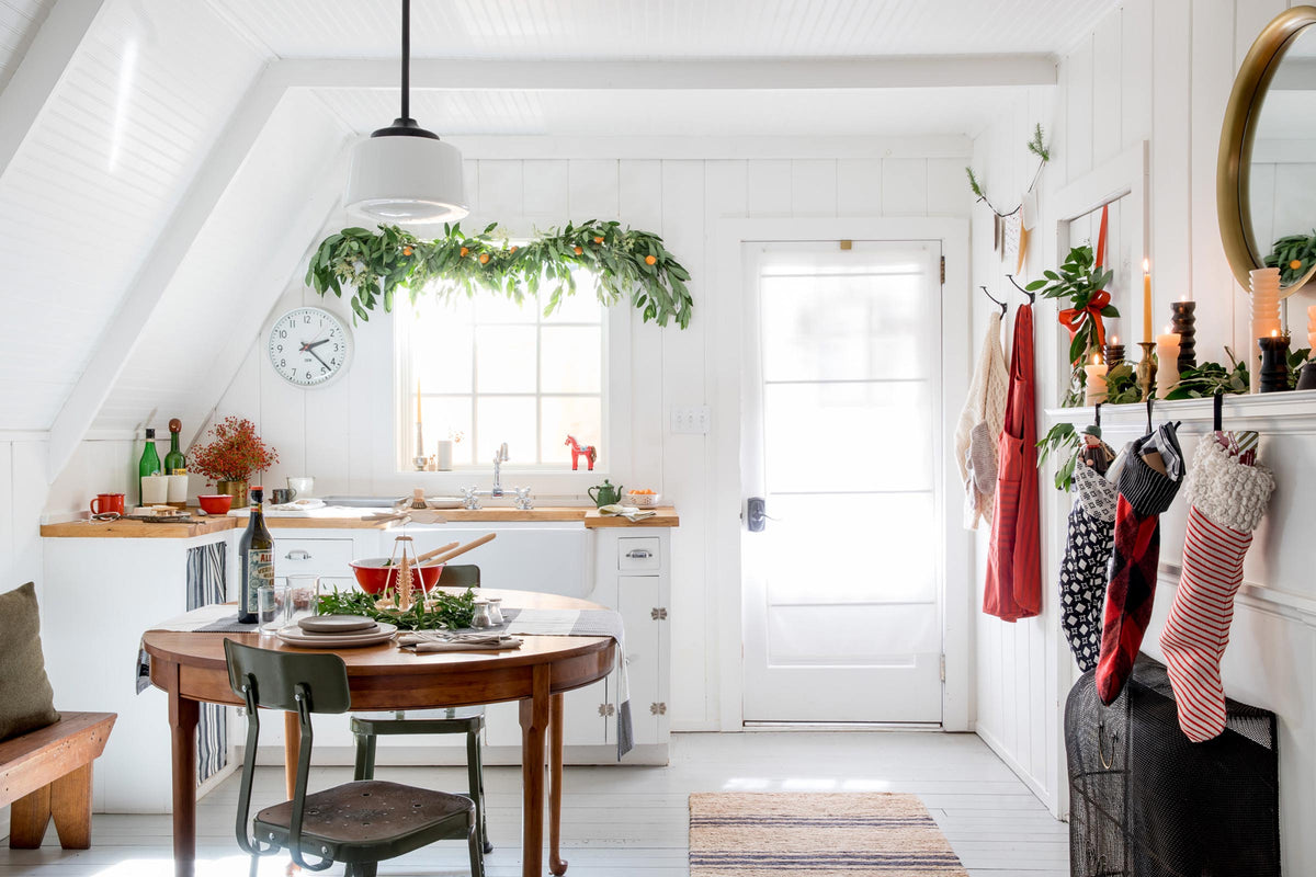 Sunlit A-frame cabin kitchen and dining area with holiday garland above the window, stockings on the mantel, and a set table