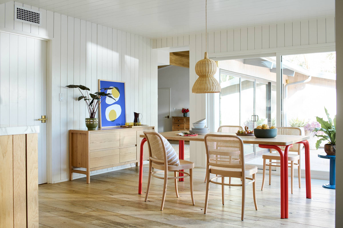 Light-filled dining room with handwoven rattan pendant over wood table with red legs and cane chairs