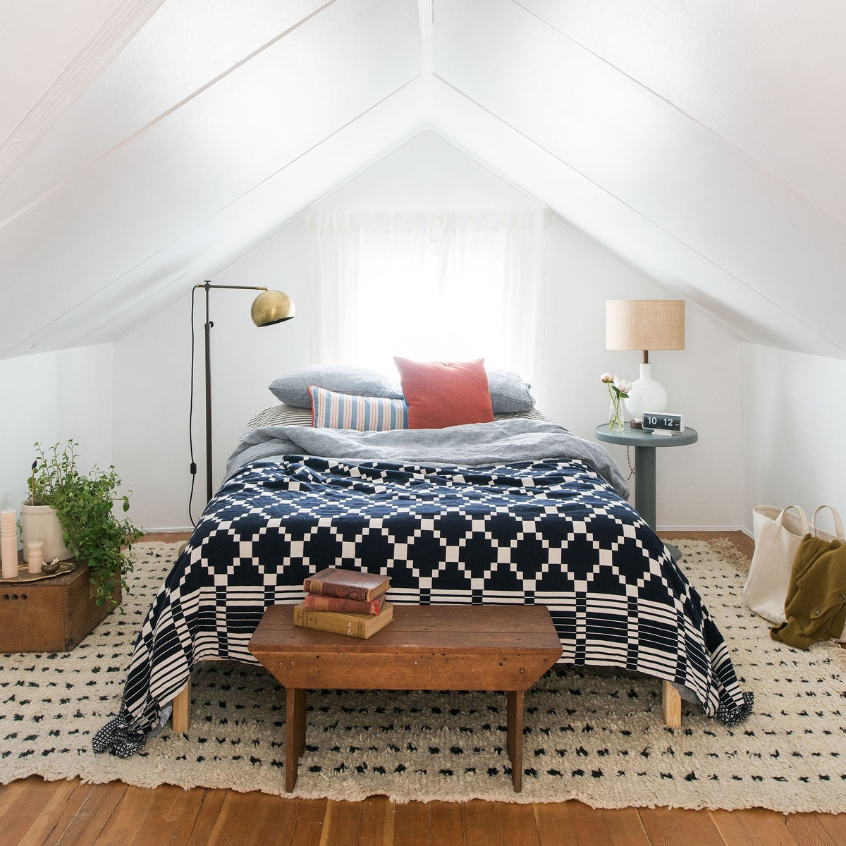 Bed topped with a navy geometric coverlet and layered pillows in a bright attic bedroom with sloped white ceiling