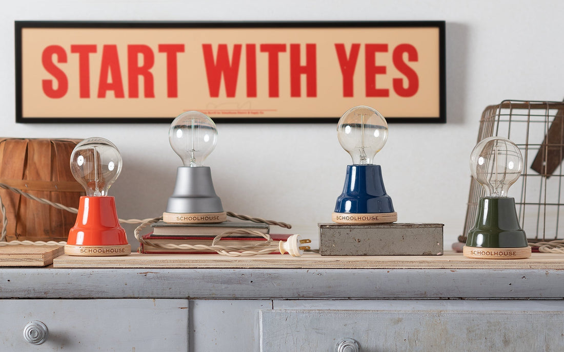 Front view of four Ion Workshop lamps showing colored enamel finishes and wood bases with START WITH YES print