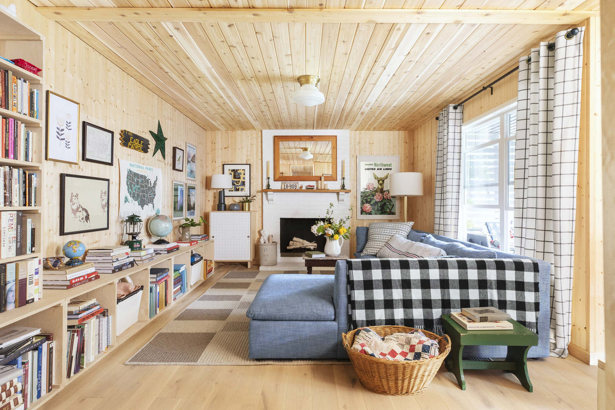 Cozy wood-paneled living room with blue sectional, fireplace, built-in bookshelves, black-and-white checkered throw and basket of quilts