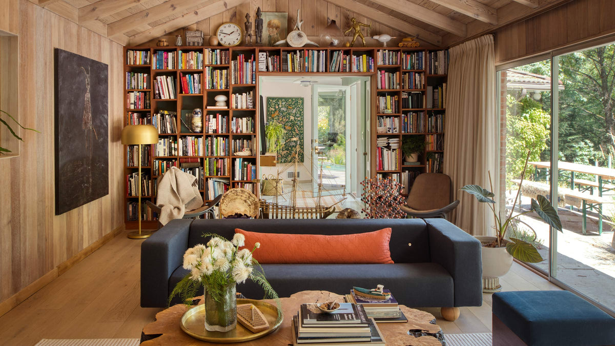 Cozy living room with built-in bookshelves behind a navy sofa, coffee table with books and flowers, glass doors to a sunlit patio