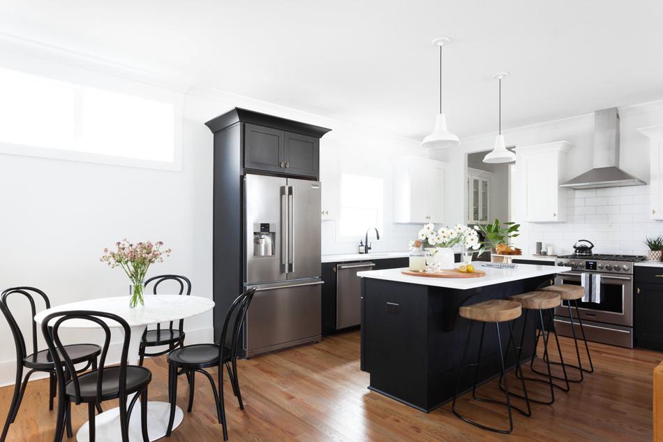 Bright modern kitchen with black island, stainless steel appliances, round white breakfast table with black chairs, and hardwood floors