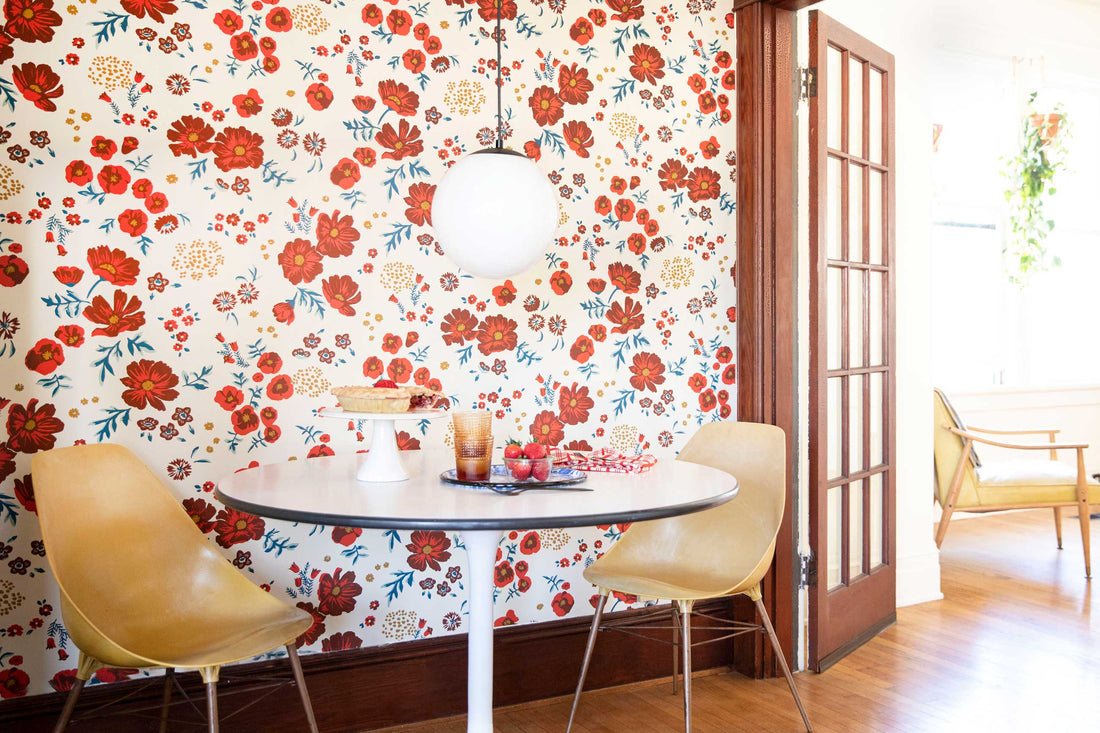 Dining nook with round white table, two yellow mid-century chairs and a globe pendant light against cream wallpaper with red floral pattern