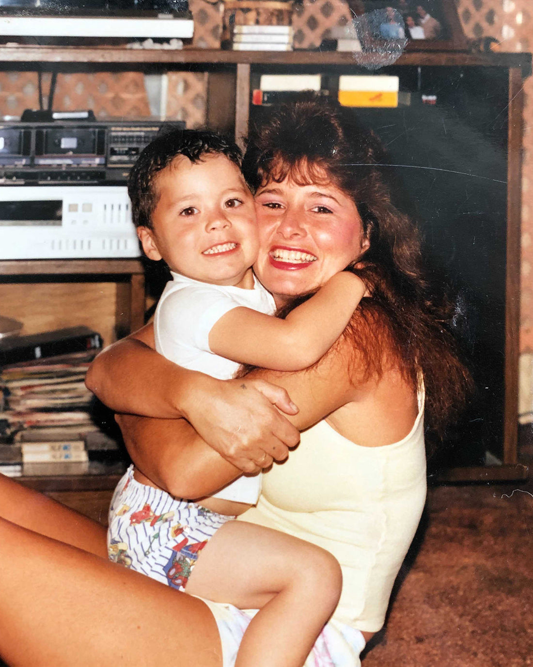 Mother hugging her young son in a cozy living room with a stereo and shelving in the background