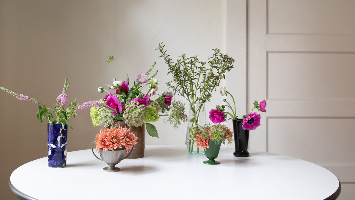 Several small mixed floral arrangements with bright pink and orange blooms on a round white table against a cream wall