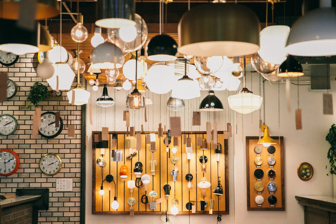 Multiple hanging pendant and globe lights illuminating a showroom with a wooden fixture sample board and wall clocks