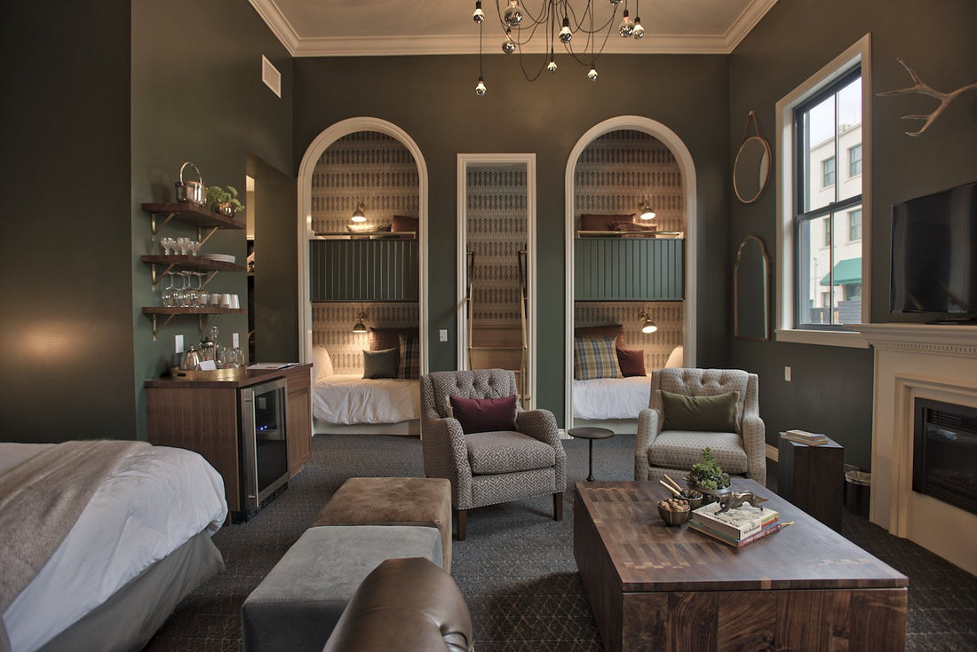 Hotel suite sitting area with two built-in arched bunk beds, upholstered armchairs, wooden coffee table, and deep green walls with a street-facing window