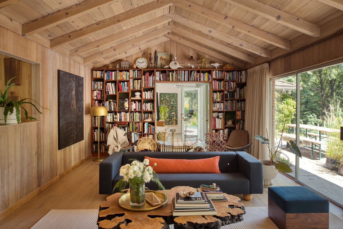 Living room with vaulted wood ceiling, built-in bookshelf behind a navy sofa, wooden coffee table, and sliding doors to a garden
