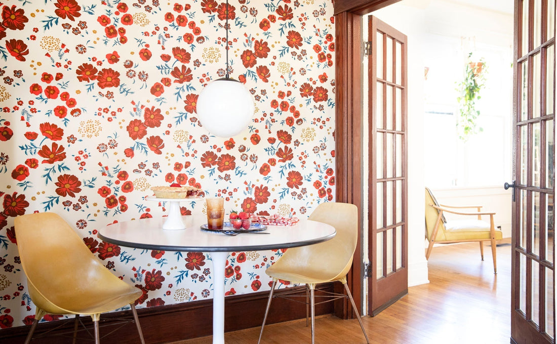 Dining nook with round table and two yellow chairs against white wallpaper with red flowers, globe pendant and wood doors