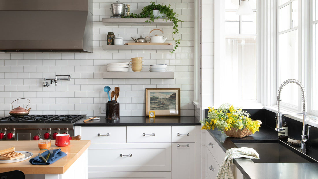 Bright kitchen with open shelves, black counters, pot‑filler over stove, and sink by sunny windows with yellow flowers