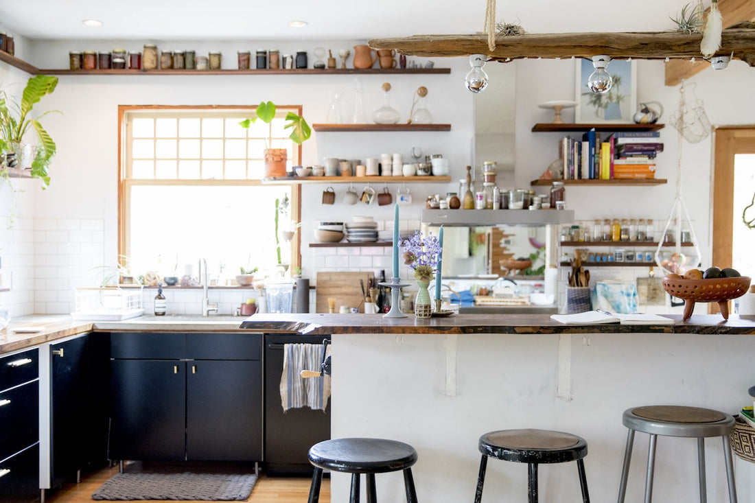 Bright airy kitchen featuring black lower cabinets, open wood shelves, a wooden island with three stools and a vase of purple flowers