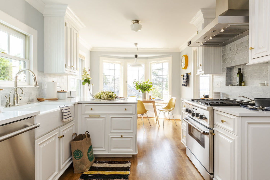 Sunlit remodeled kitchen with white cabinets, marble tile backsplash, stainless steel range, farmhouse sink, and bay-window breakfast nook