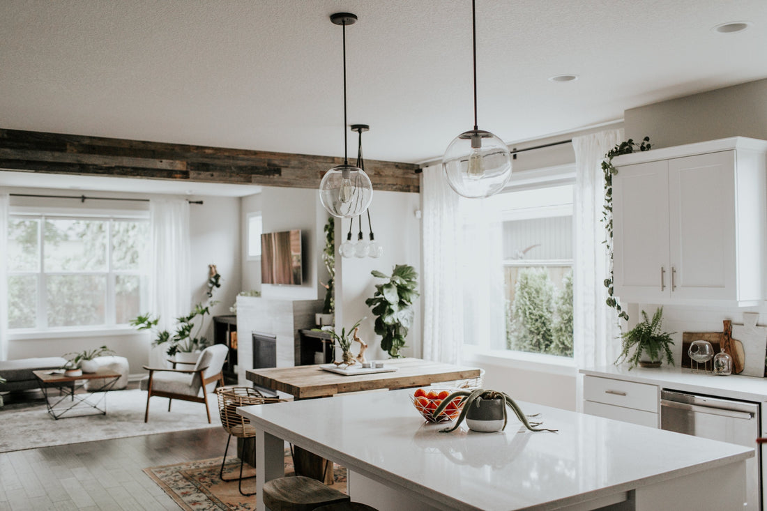 Open-plan kitchen and living area with white island, wood dining table, glass globe pendant lights, large windows and houseplants