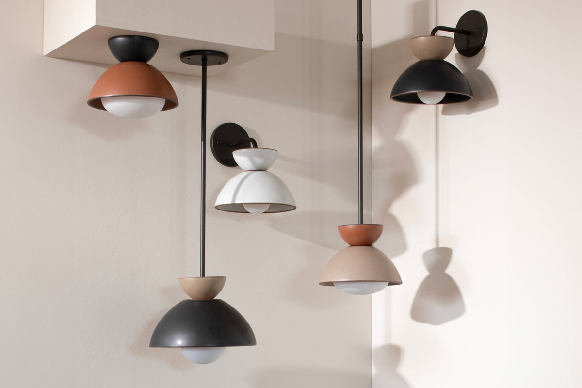 Front view of pendant lights and wall sconce showing matte terracotta, black, beige, and white finishes on a pale wall