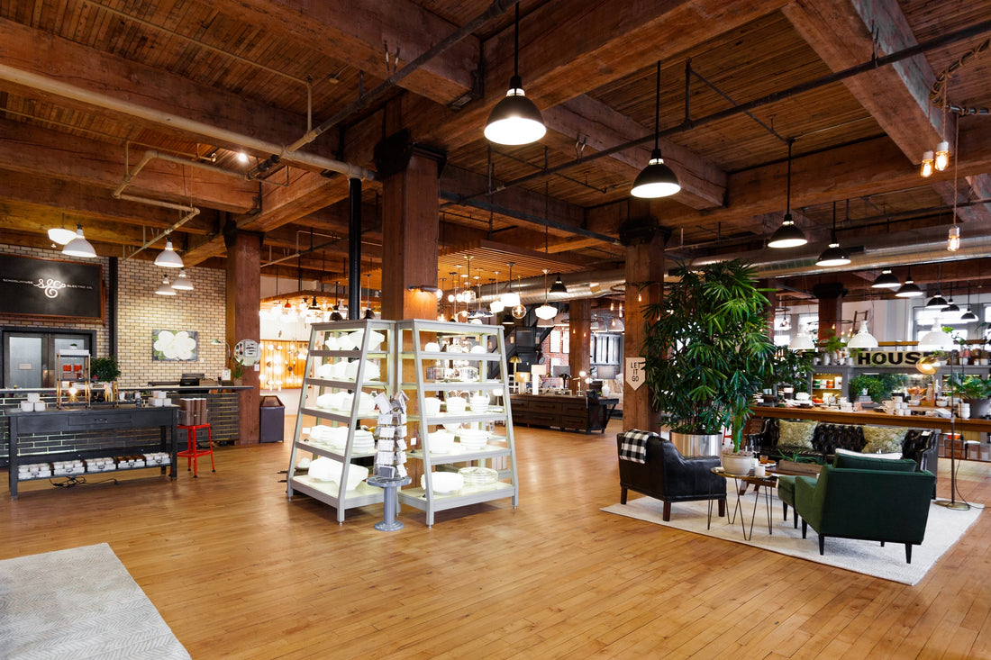 Open-plan Portland showroom with exposed timber beams, central shelves of dishware, seating area, and pendant lights