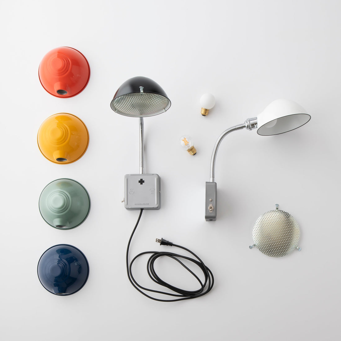 Top-down view of lamp parts showcasing colored metal shades, two gooseneck wall lamps, bulbs, and a coiled cord on a white background