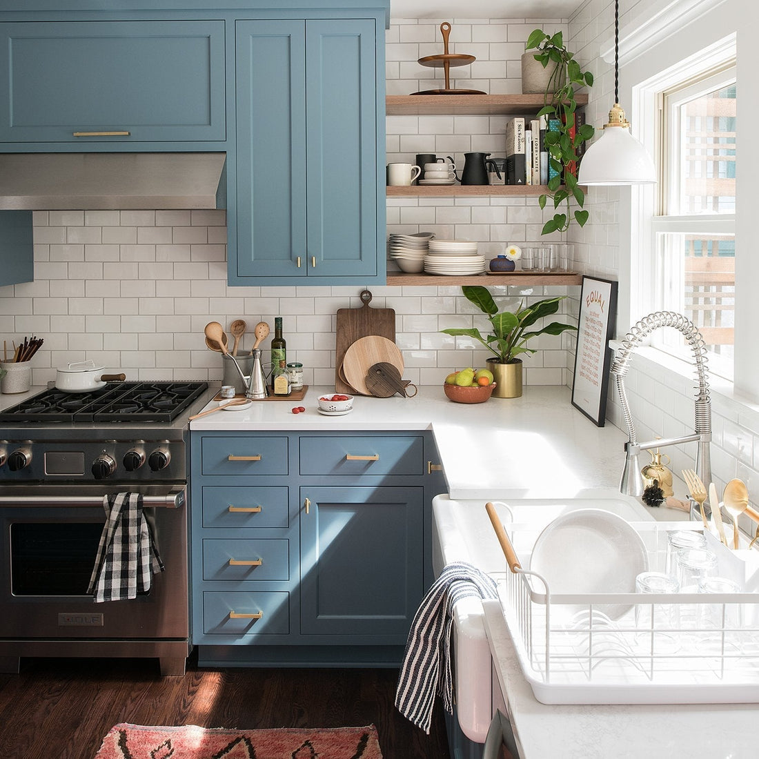 Sunlit kitchen with blue cabinets and open wood shelves, white subway tile backsplash, farmhouse sink and styled countertop