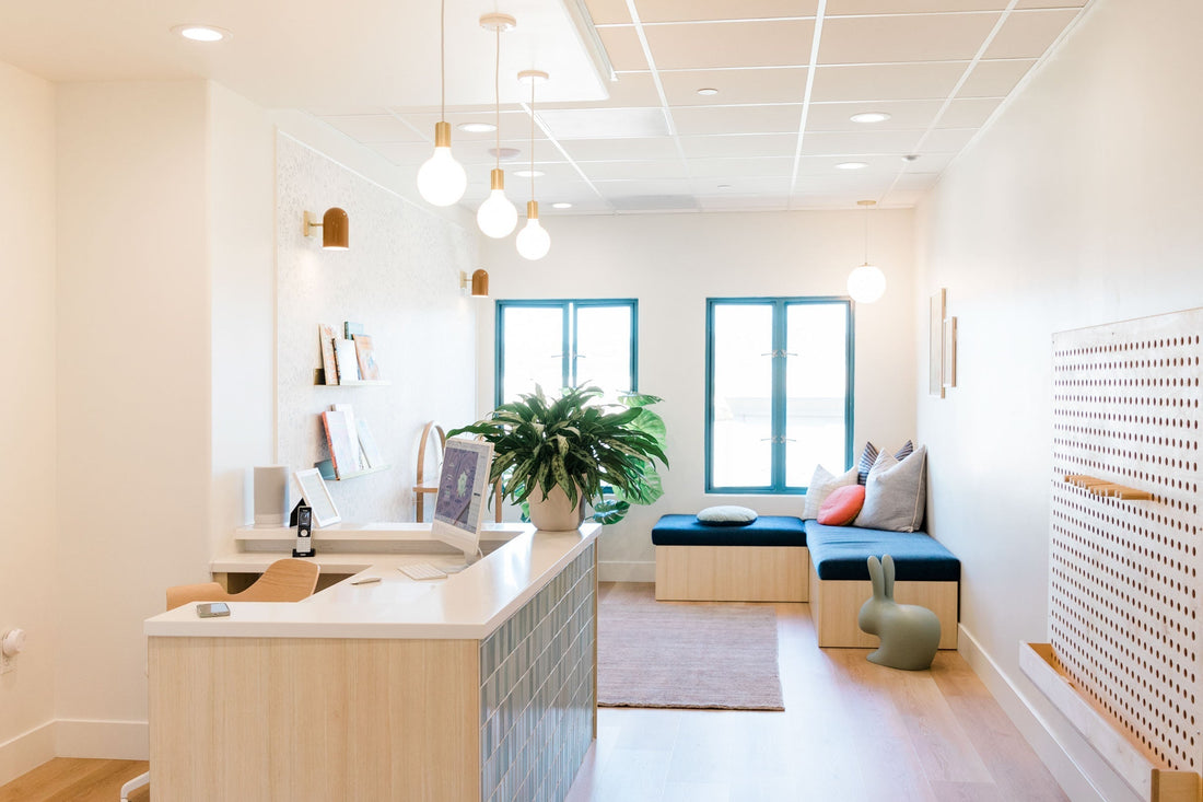 Bright pediatric dental reception with desk, pendant lights, teal windows, plant, and cushioned bench seating