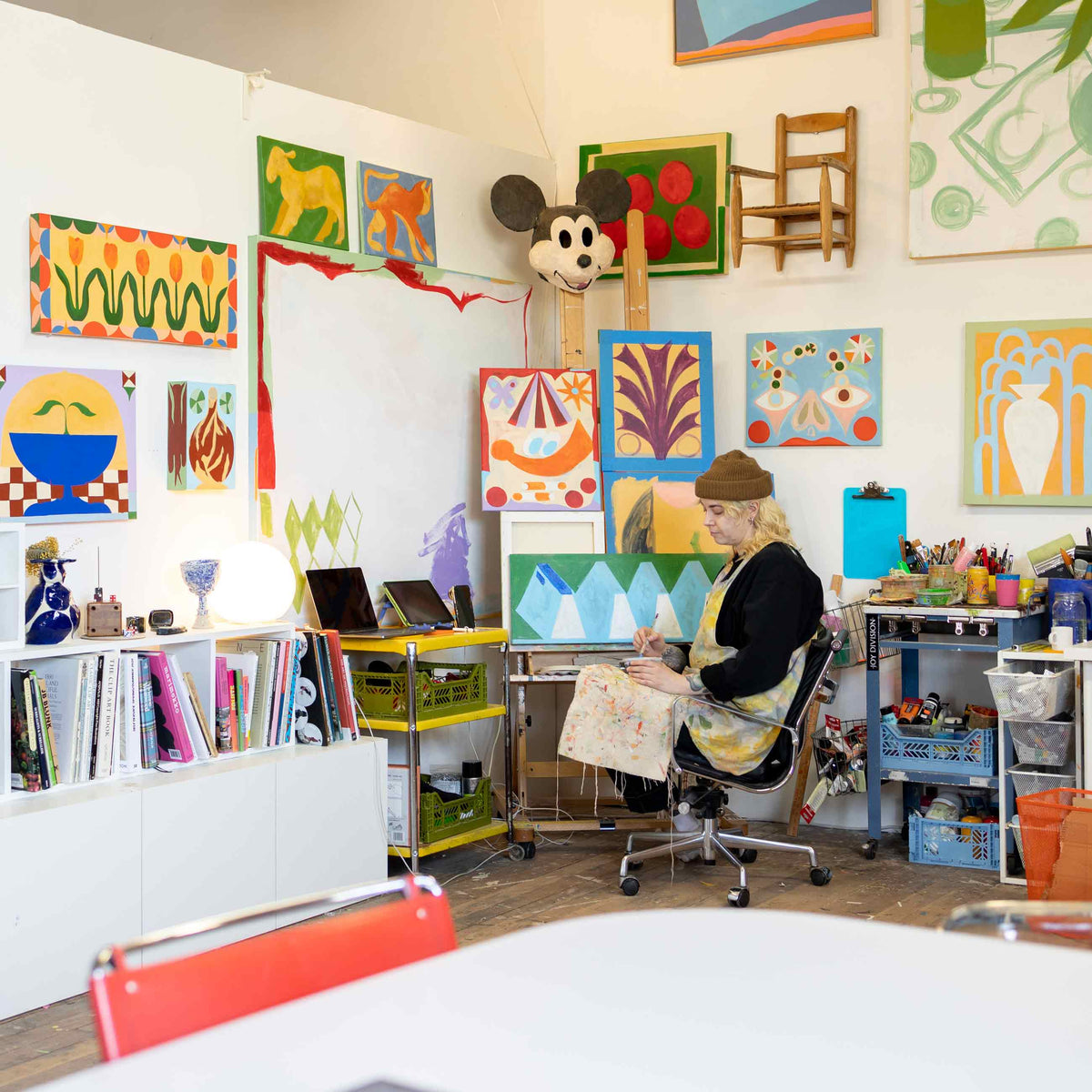 Artist Jess Ackerman painting in her bright, colorful studio surrounded by small abstract canvases and art supplies