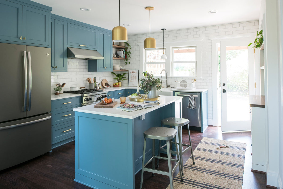 Bright kitchen with blue cabinets, brass pendant lights, white subway tile, marble island, stainless appliances, and metal stools