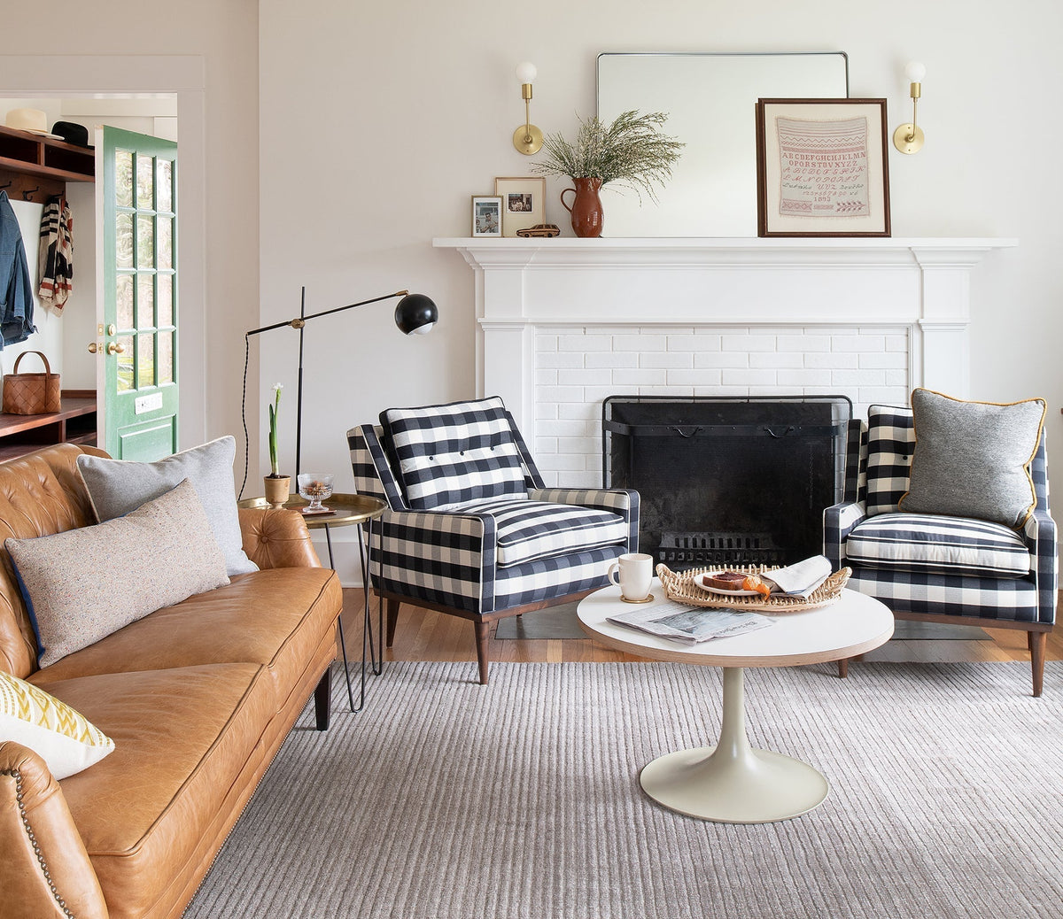 Living room with tan leather sofa and two black-and-white check armchairs around a white tulip coffee table and fireplace