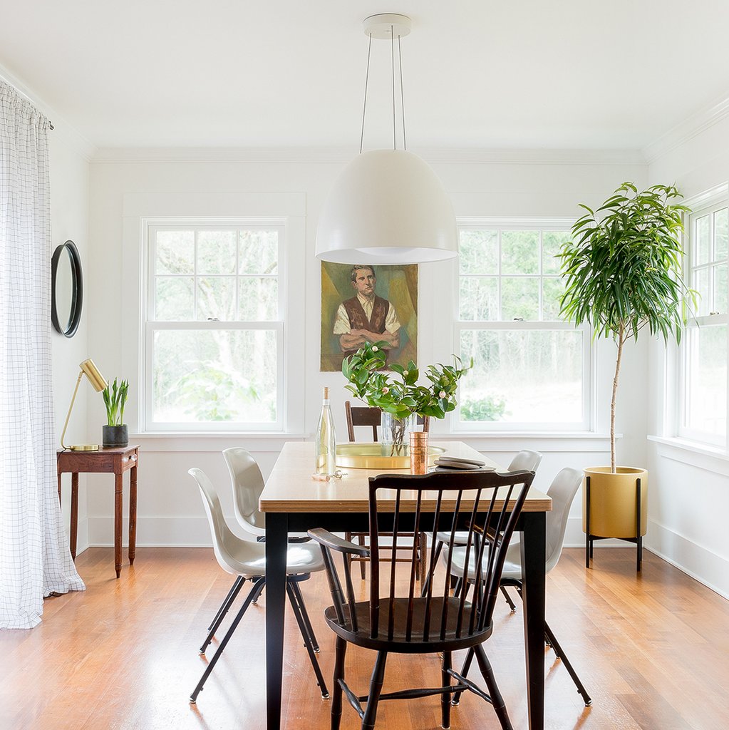 Ostara pendant hanging over a wood dining table in a bright white dining room with mixed chairs and potted plants