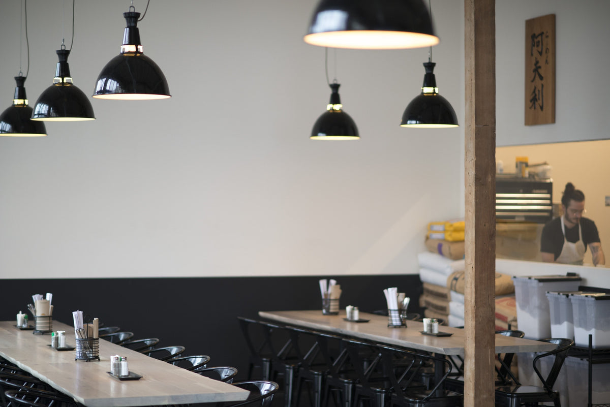 Communal wooden tables and black pendant lights in Afuri Ramen interior with a chef working behind the counter