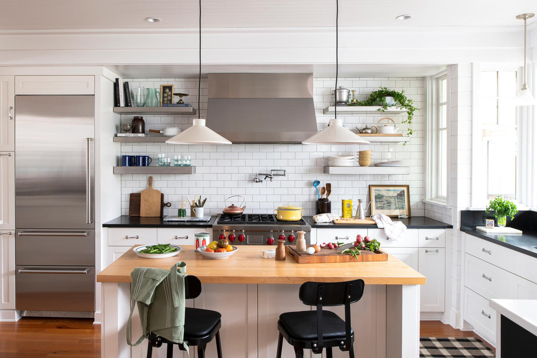 Sunlit kitchen with a wood island and stools, subway tile backsplash, stainless refrigerator, pendant lights and open shelves