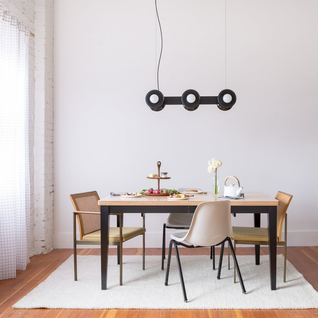 Regent three-light pendant chandelier hanging above a dining table set in a minimalist dining room with mixed chairs