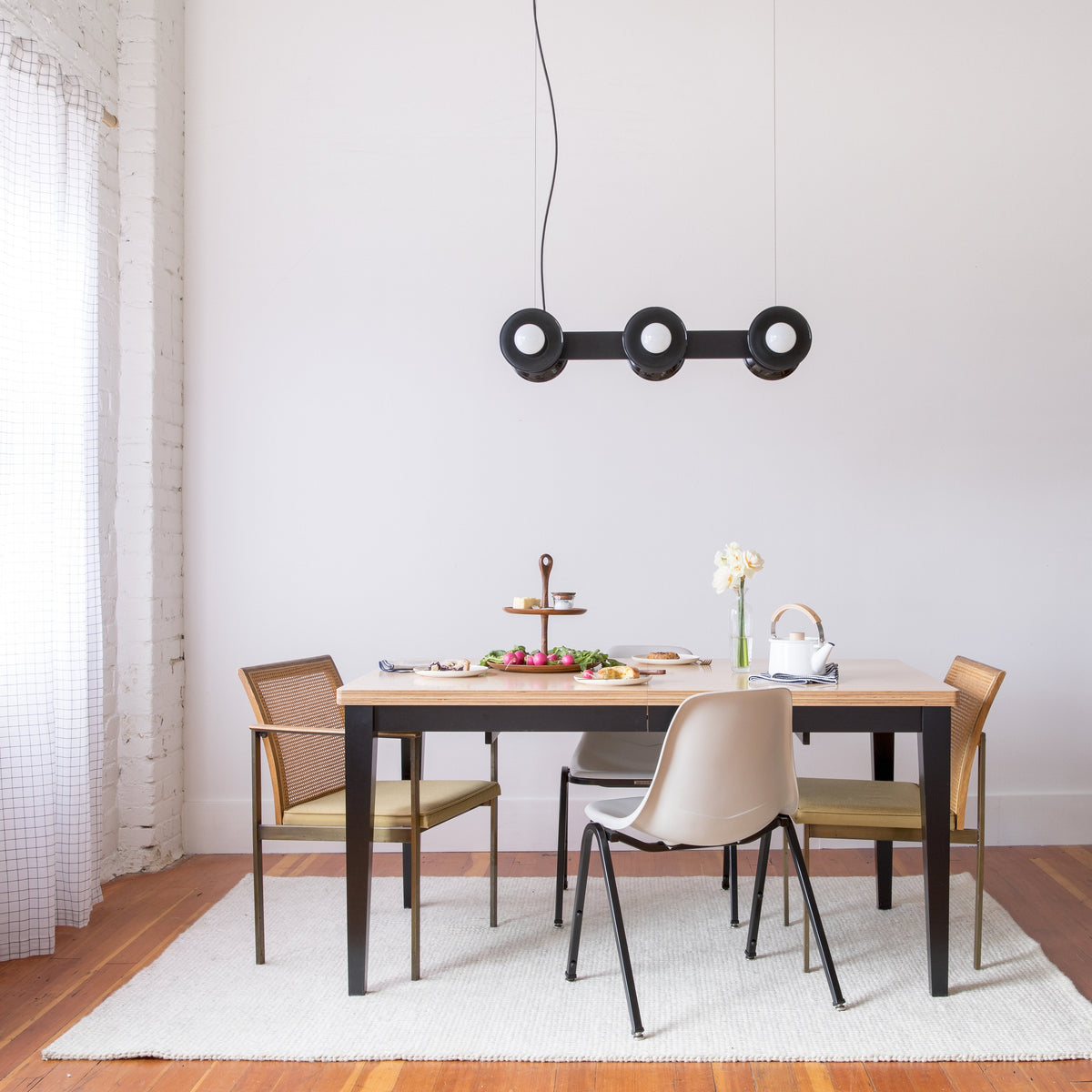 Regent three-light pendant chandelier hanging above a dining table set in a minimalist dining room with mixed chairs